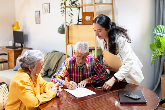 Senior couple meeting with financial advisor at home signing documents