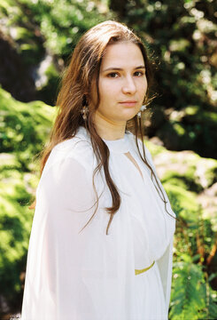 Portrait of a woman in a flowing white gown standing amid lush greener
