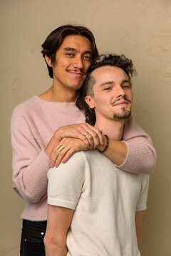 An interracial gay couple leans on each other looking at the camera