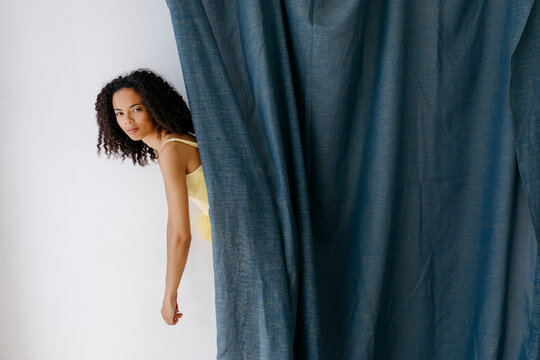 Young dancer hiding behind blue curtain in studio