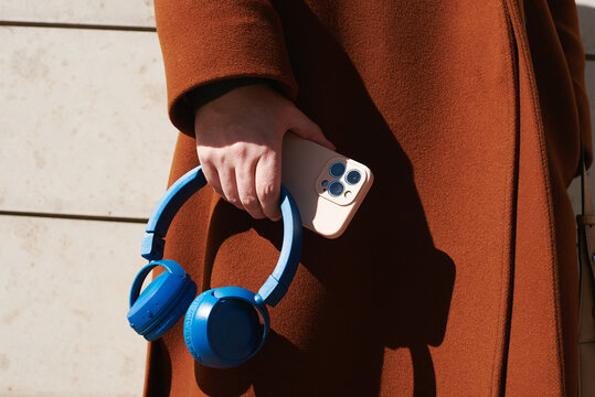 Stylish person holding phone and headphones in urban setting
