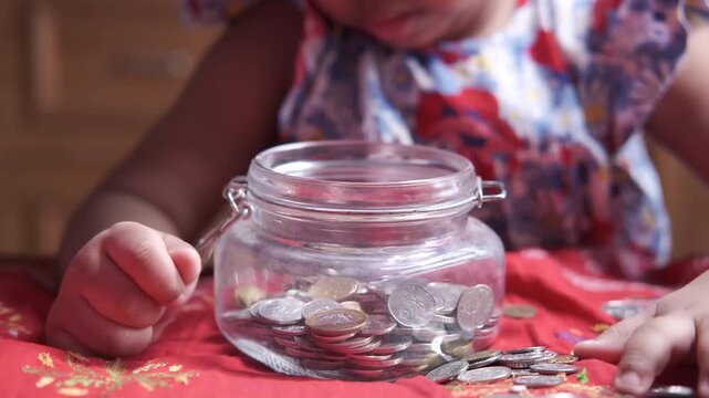 Little girl putting coins into glass jar on table to save money for future