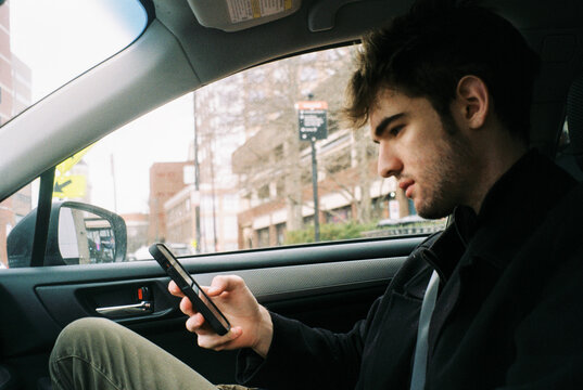 Film photo of teen riding in car looking at phone