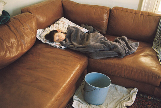 Sick child on couch at home with puke bucket nearby