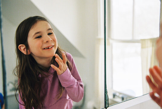 Child wiggles her loose tooth in the bathroom mirror at home