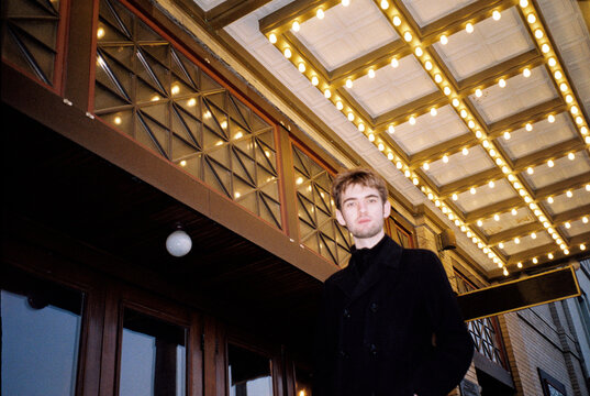 Point and shoot film photo of man walking by theatre marquee in a city