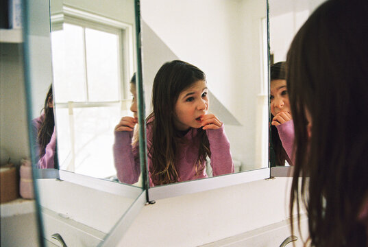 Child wiggles her loose tooth in the bathroom mirror at home