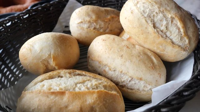 Close up video of freshly baked bread rolls in basket, golden brown crust, fluffy interior, inviting warmth, appetizing aroma, breakfast staple