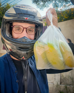 A guy wearing a helmet and pink glasses delivers a bag of mangoes