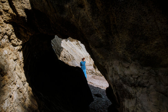 A woman lost in deep thought before a sea cave.