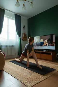 Young woman doing online yoga class at home watching tutorial on tv