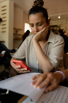 Businesswoman reading documents and holding smartphone in cafe