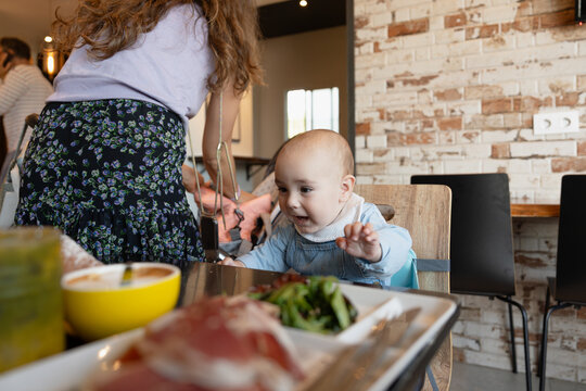 Baby grabbing food in high chair at restaurant