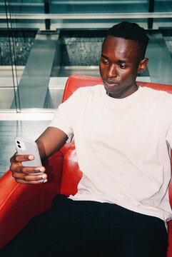 Film photo Man Sitting in Red Chair Using Smartphone