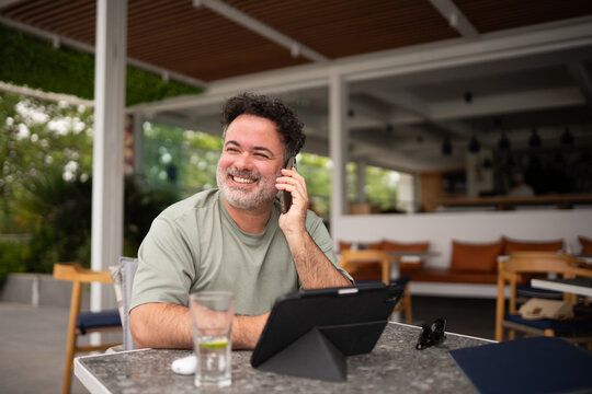Smiling Man Using Phone And Tablet in Garden Terrace