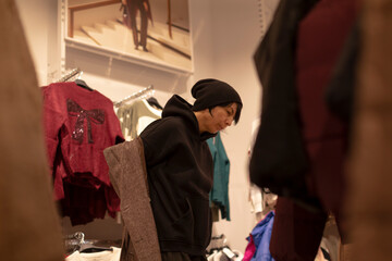 Woman shopping jackets, Customer searching for outerwear, Lady exploring clothing racks for jackets, Woman carefully examining various jackets while standing amidst busy clothing store © Viktar
