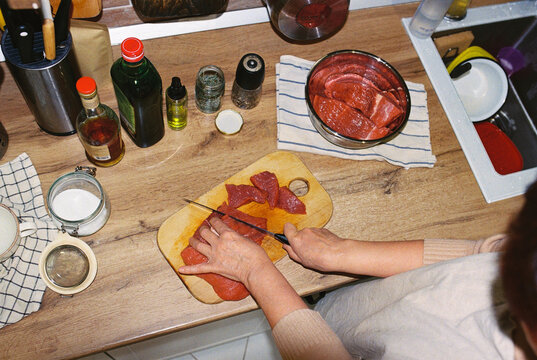 Anonymous senior woman hands cutting beef on a cutting board.