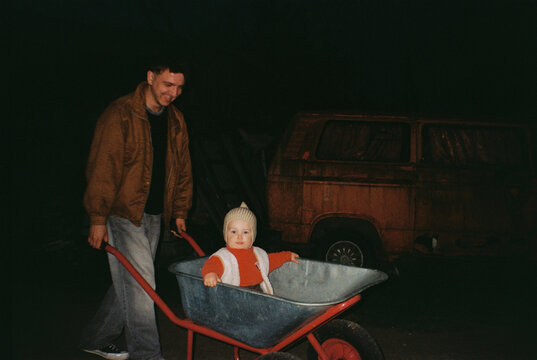 Child in a wheelbarrow pushed by smiling man - film analog