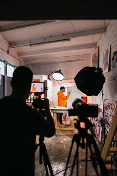Artist painting in a studio under filming lights