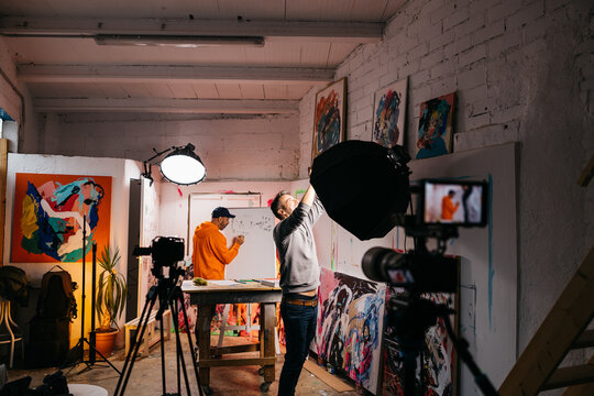filmmaker adjusting studio light while artist draws
