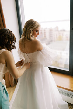 Bride Preparing for Wedding with Friend by Large Window