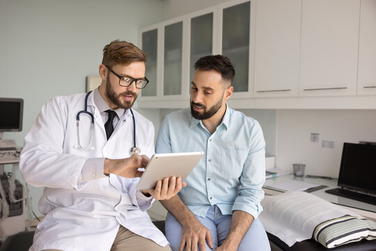 Digital tools for healthcare education. Focused male doctor medical worker discuss therapy plan with patient using electronic pad explain medical information interpret diagnostic data on device screen