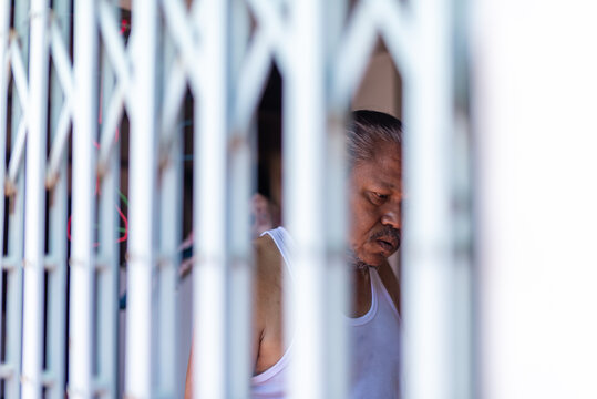 Elderly man seen through iron gate in quiet reflection