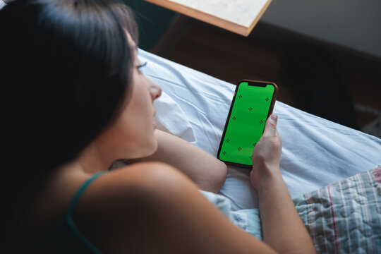 Young latina student relaxing in bed using smartphone