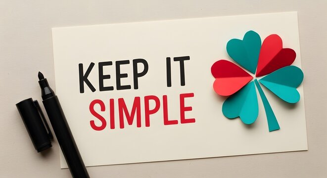 Motivational message reminding viewers to keep it simple alongside a colorful paper clover design and a nearby black marker on a neutral surface.