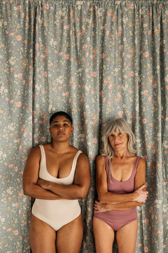 portrait of two women in bodysuits standing with arms crossed
