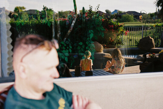 Father watches kids sitting by pool during family vacation