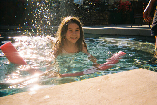 Happy girl swims in pool with noodle