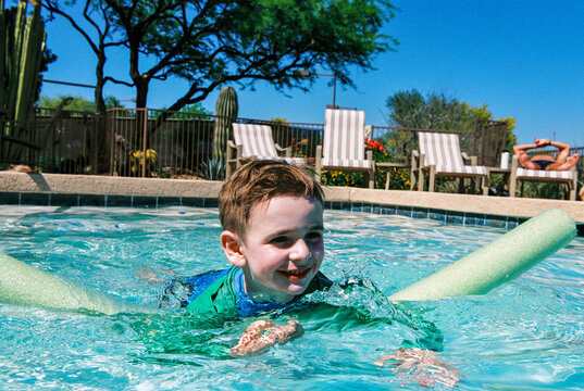 Happy child swimming in hotel pool with noodle