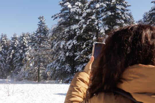 Young woman in winter forest taking pictures