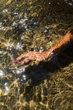 Hand touching sparkling water in a serene natural setting