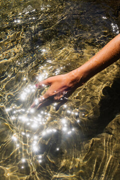 Hand touching sparkling water in a serene natural setting