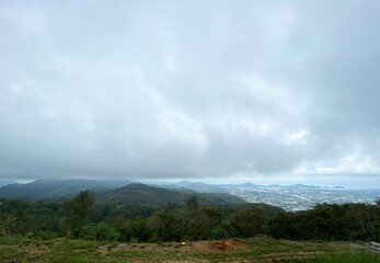 Obraz premium Scenic view of lush green hills and distant coastline under cloudy sky in Phuket, Thailand, showcasing the natural beauty of the region's landscape