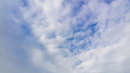 Fototapeta premium High wide‑angle view of the sky filled with rippled white clouds drifting across a pale blue backdrop, creating a light, airy pattern that suggests gentle winds and spacious calm above the landscape
