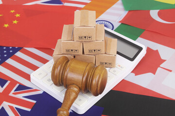 Many cardboard boxes with calculator on different national flags and judge gavel. Global trading, laws and tariffs concept.