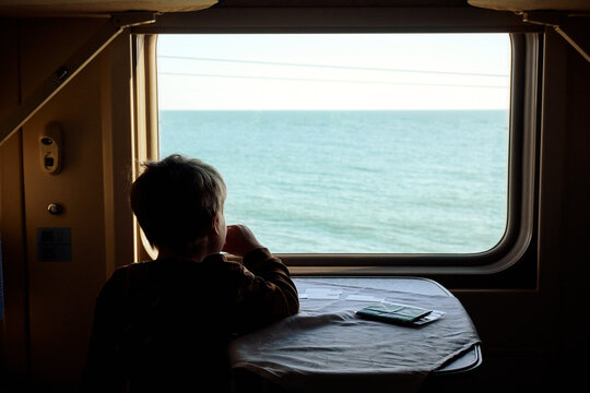 Boy sits on a train in front of a window overlooking the sea