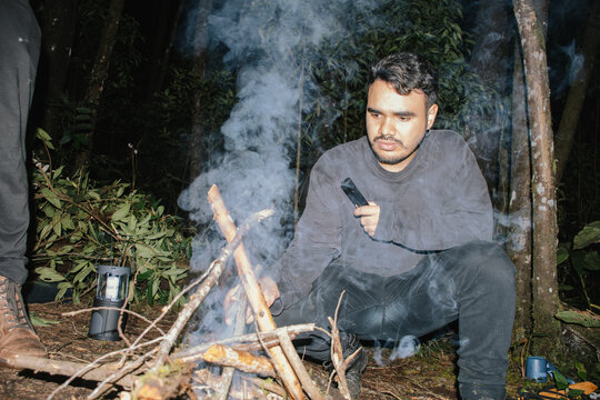 Man tending to a Campfire in a forest during nighttime gathering