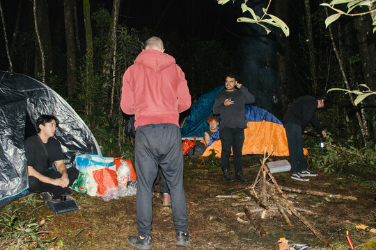 Group camping in a forest at night with tents and a campfire