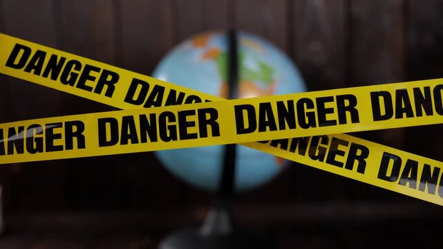 Close-up of a globe on a dark wooden background. In the foreground, there is a yellow warning tape with the inscription DANGER. World problems, ecology, and protection of the planet are discussed.