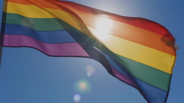 Rainbow Pride Flag Waving In The Blue Sky With Sunlight