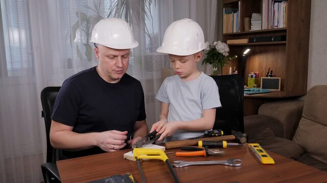 A man with a bald head and wearing a white helmet instructs his son on the art of repair, demonstrating various tools for maintenance. The father and son enjoy their time together.