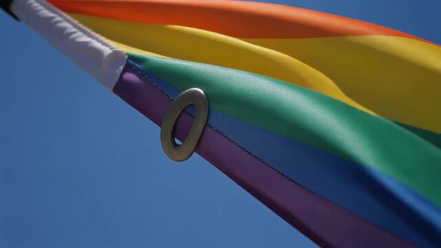 Close Up Of Rainbow Pride Flag Waving Against Blue Sky
