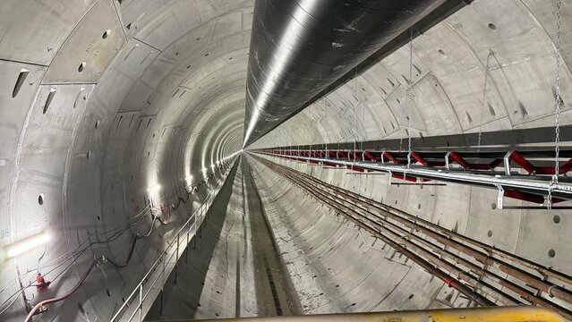 Railway tunnel excavation through mountainous terrain on line LK104 using TBM technology. Tunnel boring machine advancing underground with installation of precast concrete segments forming the tunnel.