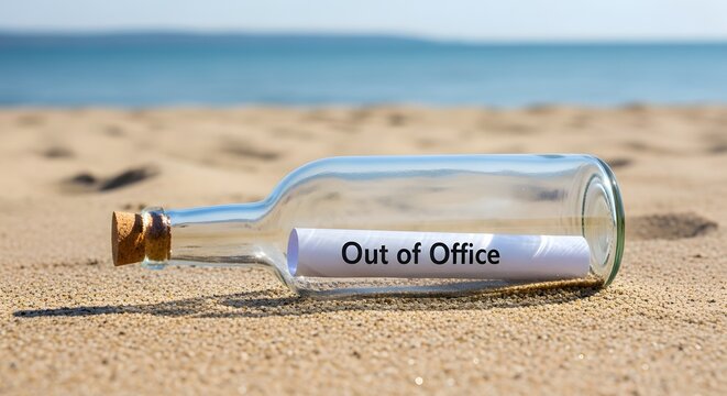 A clear glass bottle with a cork stopper and a message inside reading out of office on a sandy beach.