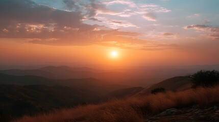 Obraz premium A breathtaking sunset casts warm golden and orange hues across layers of hazy mountain ridges under a soft cloudy sky