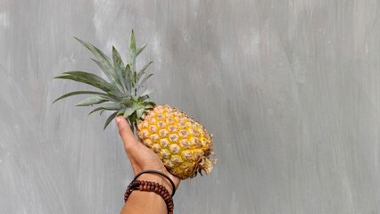 Hand holding fresh pineapple against plain background, tropical fruit and healthy food concept....